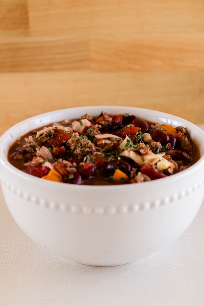 Bowl of deer chili on white counter with a wooden back splash.