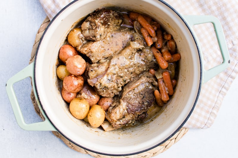 Dutch oven roast in a cast iron enameled dutch oven on a white marble countertop.