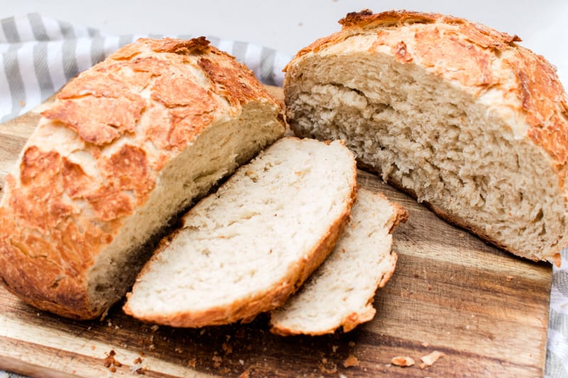 Homemade artisan bread, sliced up on a wooden cutting board.