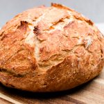 Dutch oven no knead bread with crispy tips on wooden cutting board.