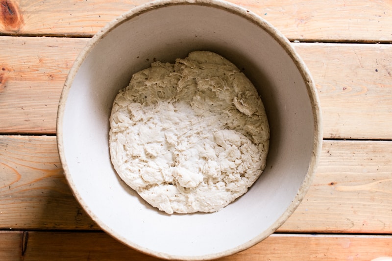 Risen bread dough in a large crock on wooden table.