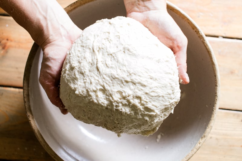 A perfectly shaped round bread loaf over a crock ready to go into the dutch oven.