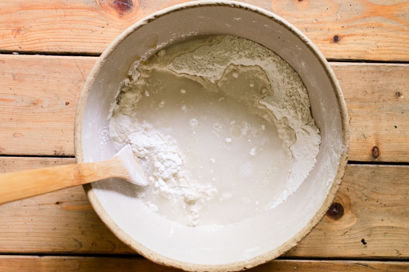 Bread ingredients in a large crock with a wooden spatula.