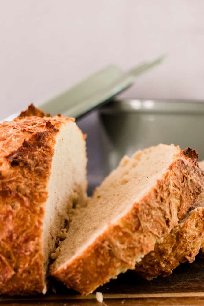 Sliced artisan bread with a green dutch oven in the background.