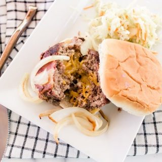Juicy lucy burger with sautéed onions on a white plate with fresh coleslaw.