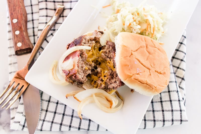 Juicy lucy burger with sautéed onions on a white plate with fresh coleslaw.