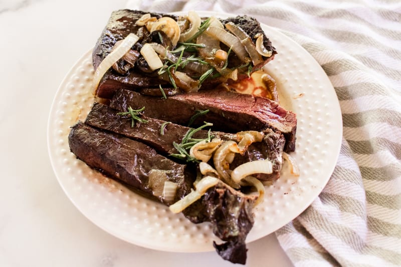 Sliced grilled beef heart on wooden cutting board with parsley sparsely scattered around it.