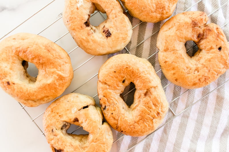 Chocolate chip bagels on a cooling rack on a white marble countertop.