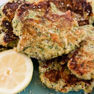Golden brown fried zucchini cakes with a sliced lemon for drizzling.