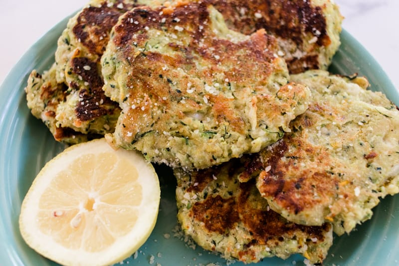 Golden brown fried zucchini cakes with a sliced lemon for drizzling.