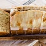Tender zucchini bread sliced on a wooden bread tray with a white glaze drizzled over the top.