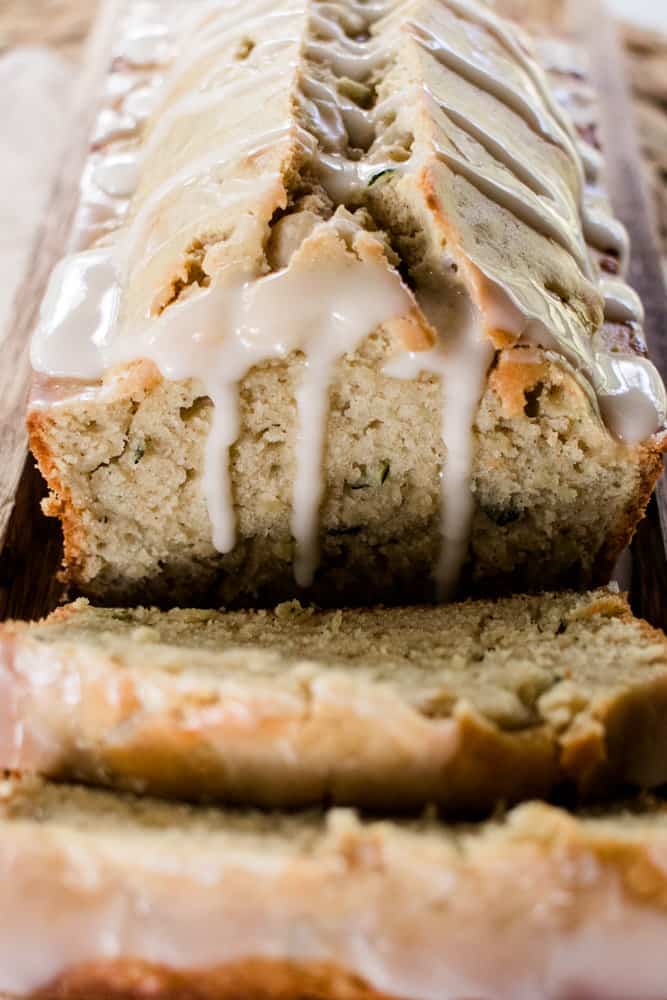 Lemon glaze dripping down the sides of a warm loaf of zucchini bread.