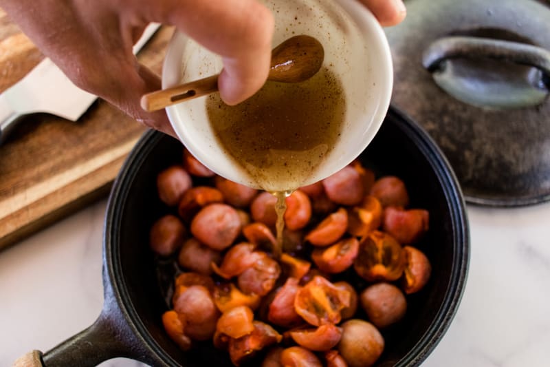 Dressing of honey, coconut oil, butter and spices drizzled on top of cast iron skillet full of baked persimmons.