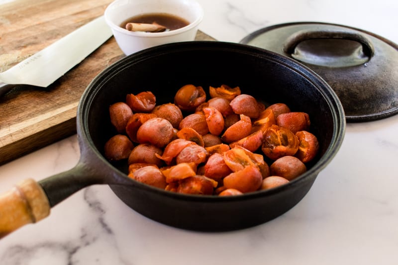 Cast iron skillet full of rustic spiced baked persimmons on a marble kitchen countertop. 