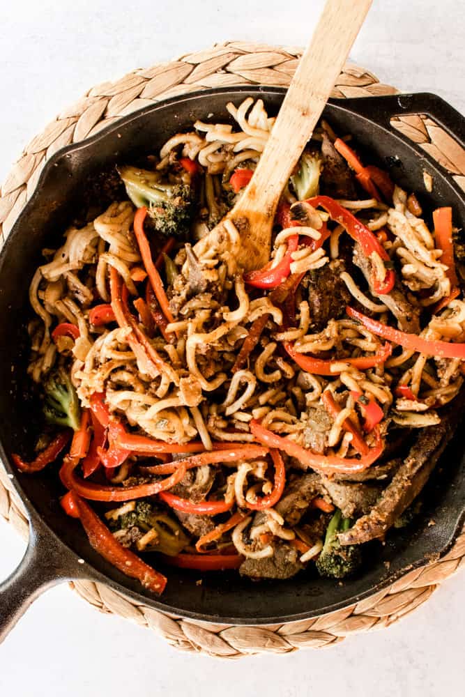 Stirring noodles into beef liver stir fry in a cast iron skillet.