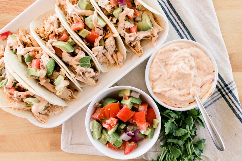 Five chipotle chicken street tacos on a plate with diced toppings and chipotle cream sauce. 