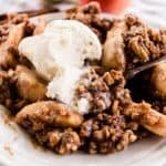 Hot baked apple crisp on a white plate with a large scoop of ice cream.