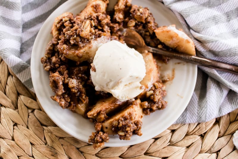 Dutch oven apple crisp topped with ice cream on a beautiful fall table.