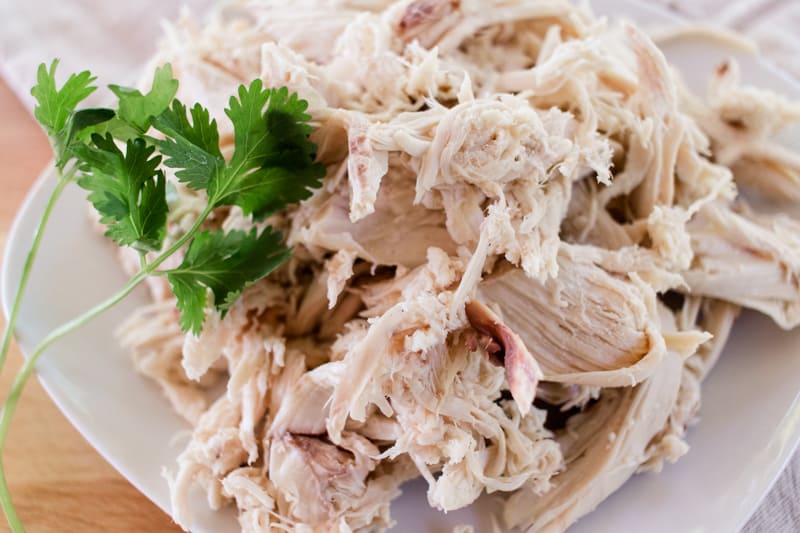 Tender shredded chicken with a sprig of parsley on a white plate, ready for your favorite recipe.