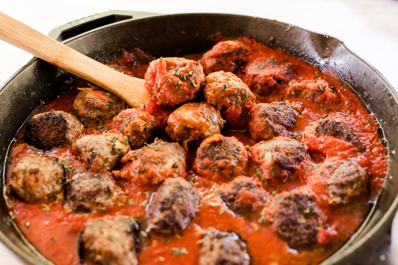 Cast iron skillet full of stovetop meatballs in marinara sauce. 