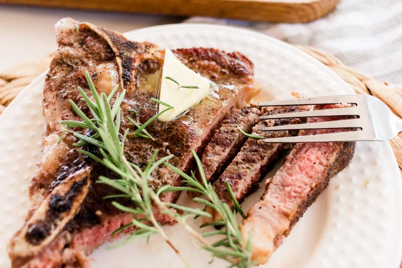 Reverse seared steak on a white serving plate with rosemary springs and a dollop of butter.