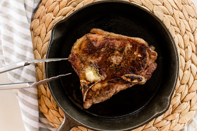 Thick cut beef steak searing in a cast iron skillet.