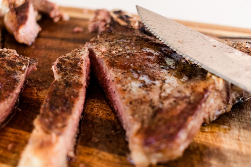 Sliced t-bone steak on a wooden cutting board.