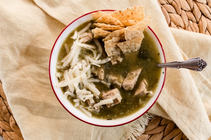 Bowl of Colorado green chili made with pork shoulder, topped with shredded white cheese and corn tortilla chips. 