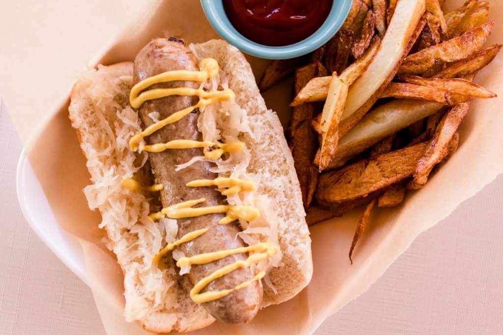 Bratwurst cooked on the stove, placed in a bun served with sauerkraut, mustard, ketchup and fries. 