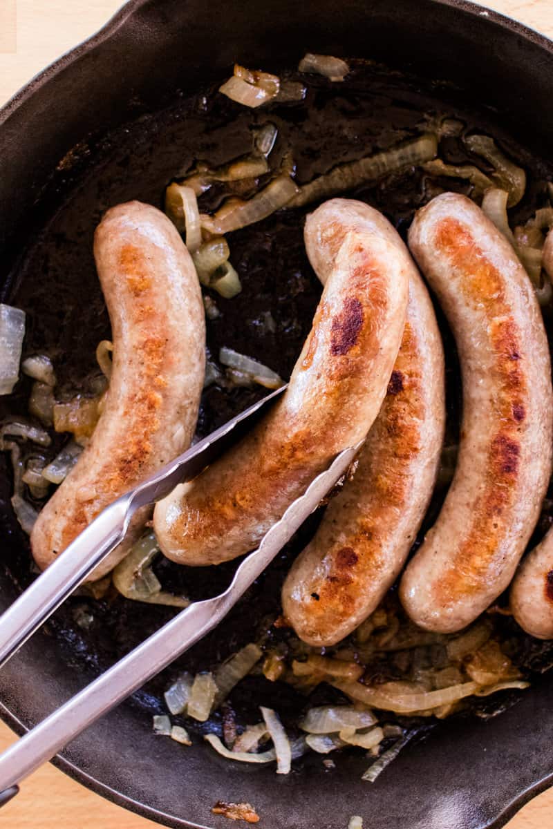 Cast iron skillet filled with seared brats cooked on the stove with onions and broth.