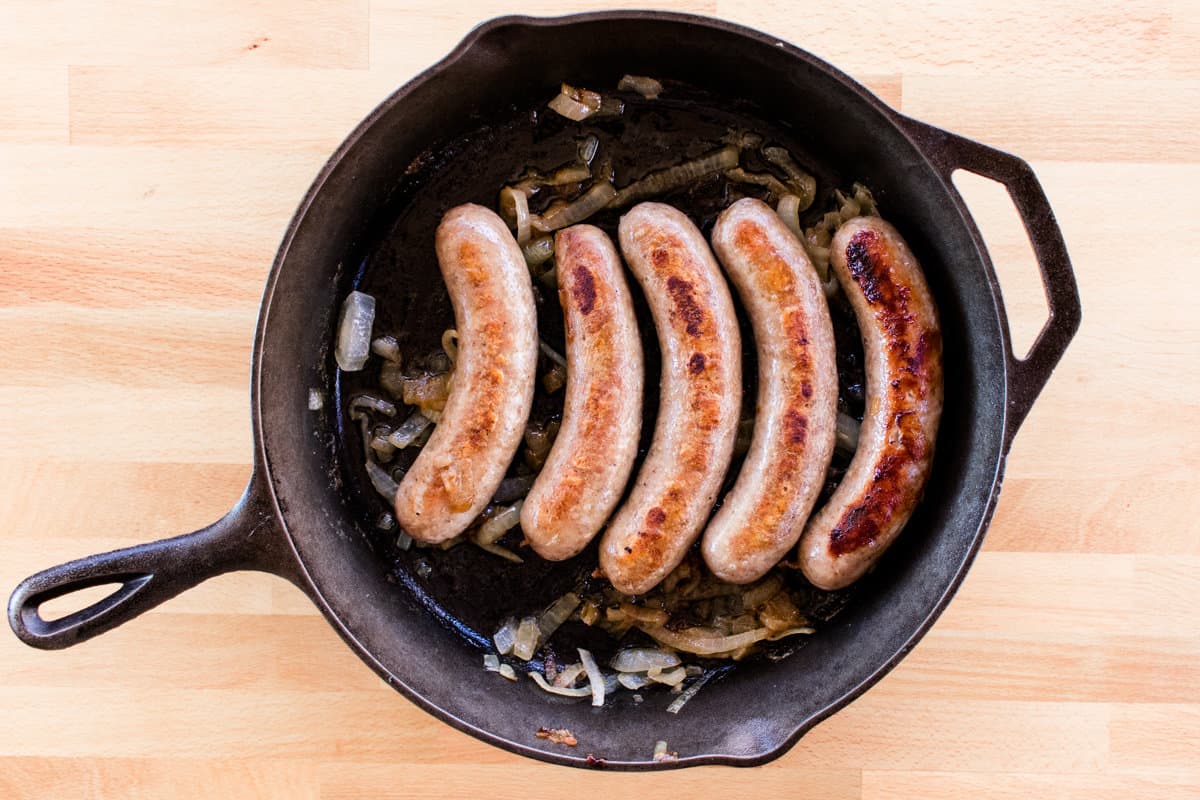 5 brats lined on a cast iron skillet. 
