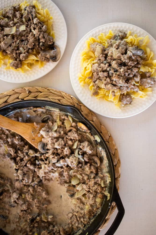 Cast iron skillet and two plates full of ground venison stroganoff. 