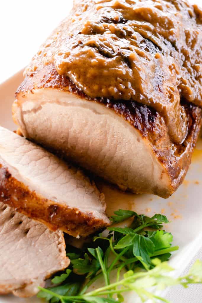 Pork loin roast cut in slices on a platter with gravy and a glaze on top. 