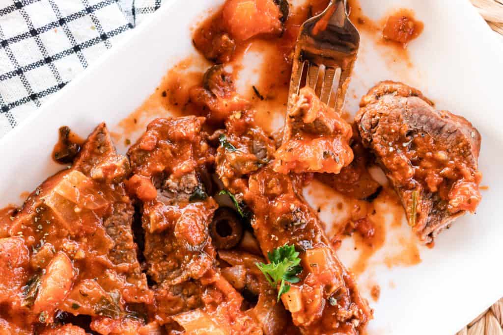 Steak in tomato sauce cut up on a white dish on a table top. 