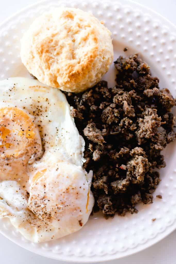 Ground venison breakfast sausage on a white plate with an over easy egg.
