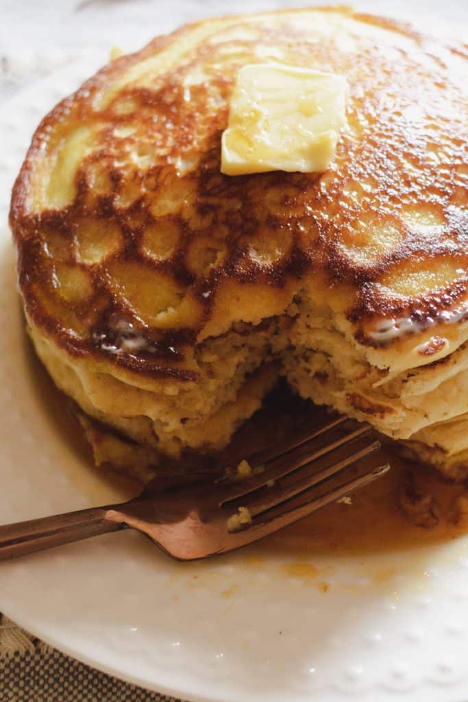 Stack of pancakes cooked in cast iron with a slab of melted butter and  maple syrup drizzled over the top. 