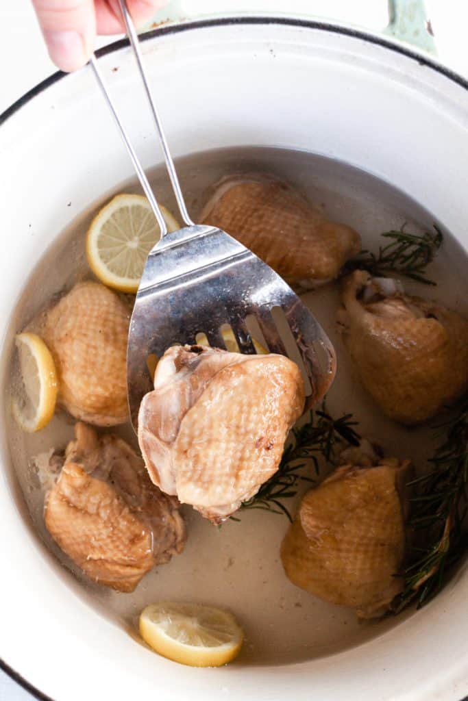 Scooping out boiled chicken from a dutch oven.

