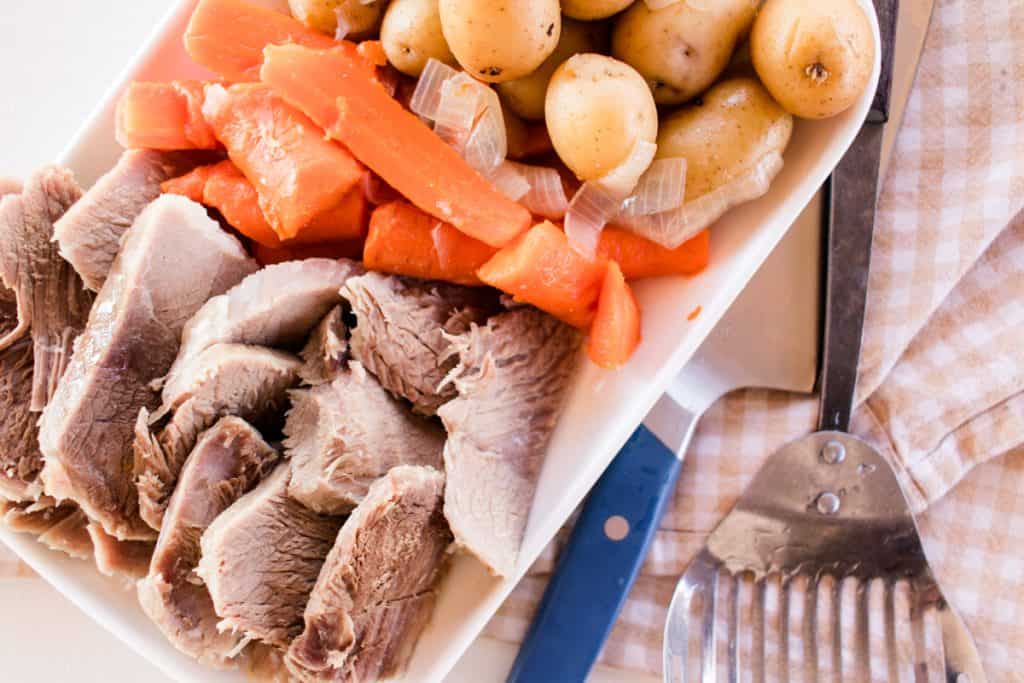 Homemade pork cottage roll with carrots and potatoes on a white serving dish.