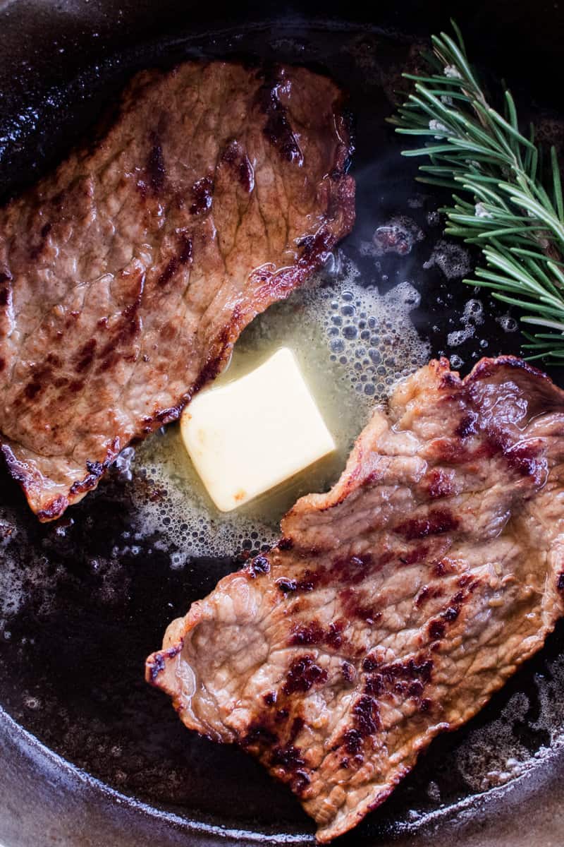 Searing bottom round steaks on a cast iron skillet with butter.