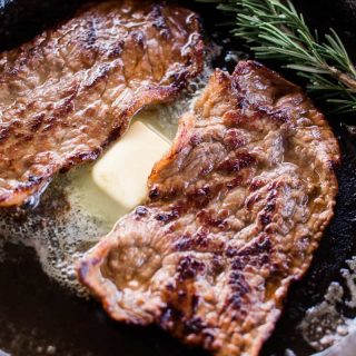 Marinaded beef round steaks sliced thin and cooking in a large cast iron skillet.