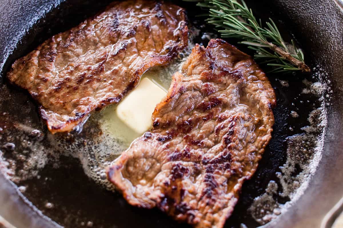 Marinaded beef round steaks sliced thin and cooking in a large cast iron skillet.