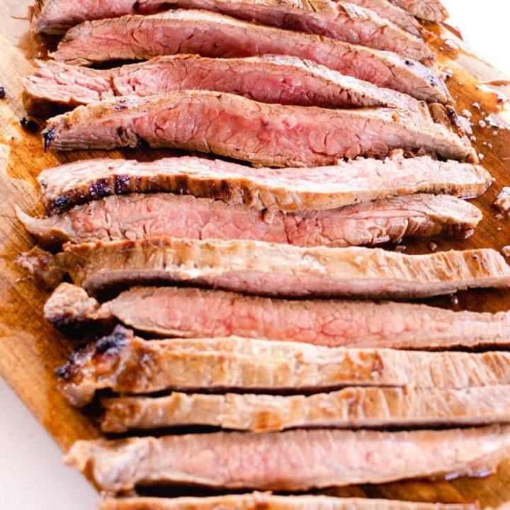 Thinly sliced cast iron flank steak on a wooden cutting board.