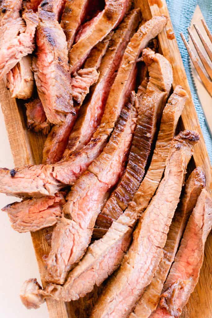 Slices of perfectly cooked flank steak filling a wooden cutting board.