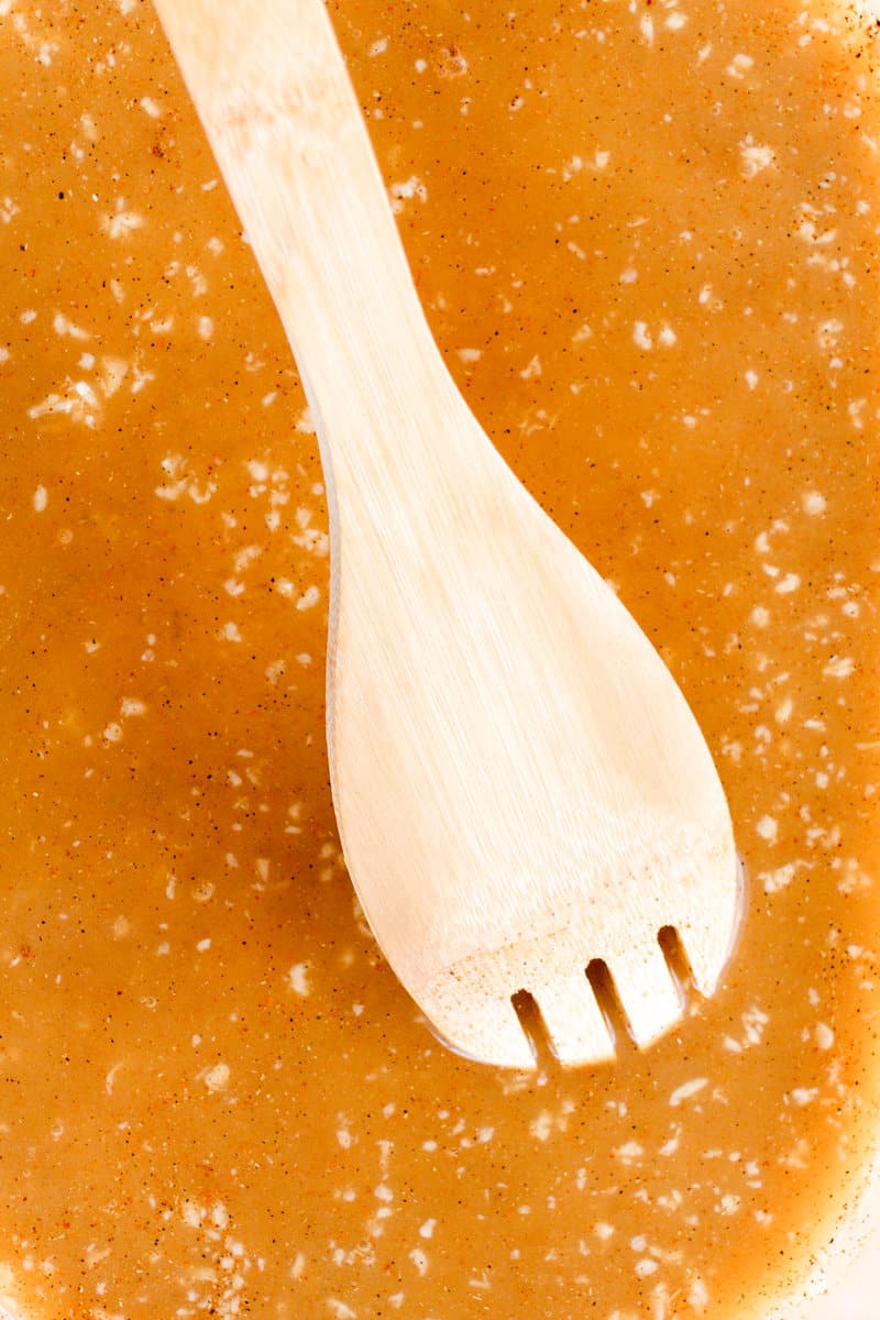 A wooden spoon mixing an orange-colored marinade.