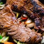 Skirt steak with a dark, crisp sear on a bed of sautéed vegetables.