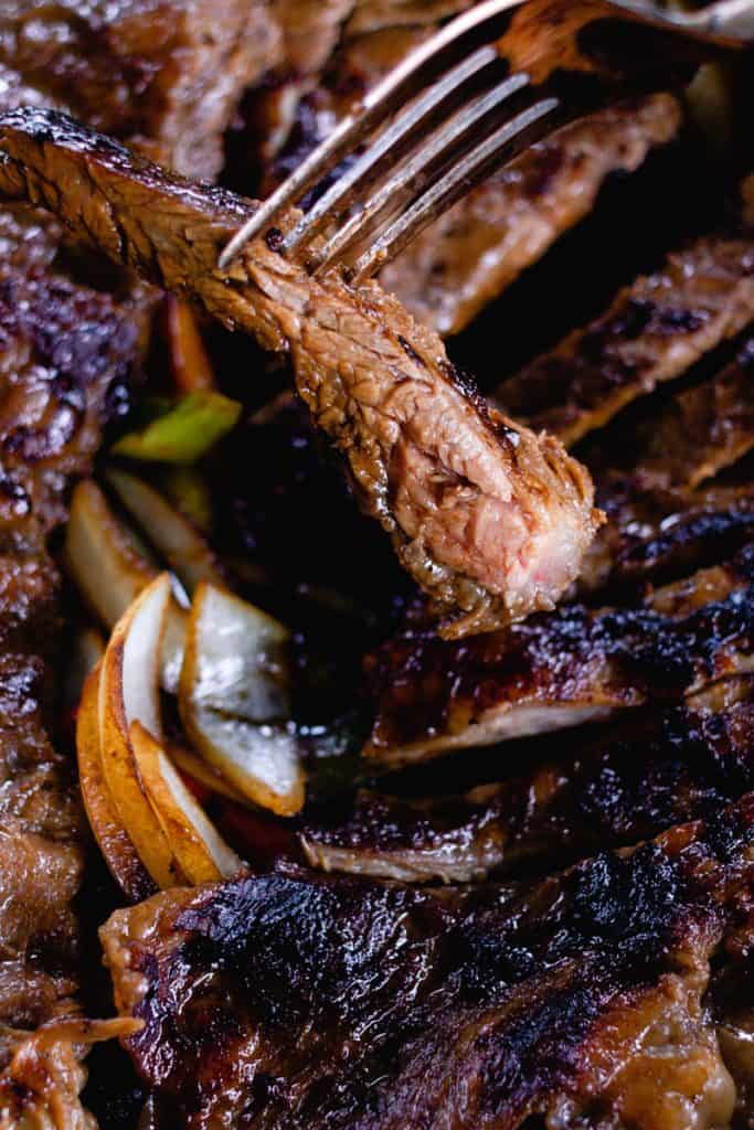 Strips of nicely browned skirt steak with vegetables, with a fork holding one delicious-looking strip of beef.