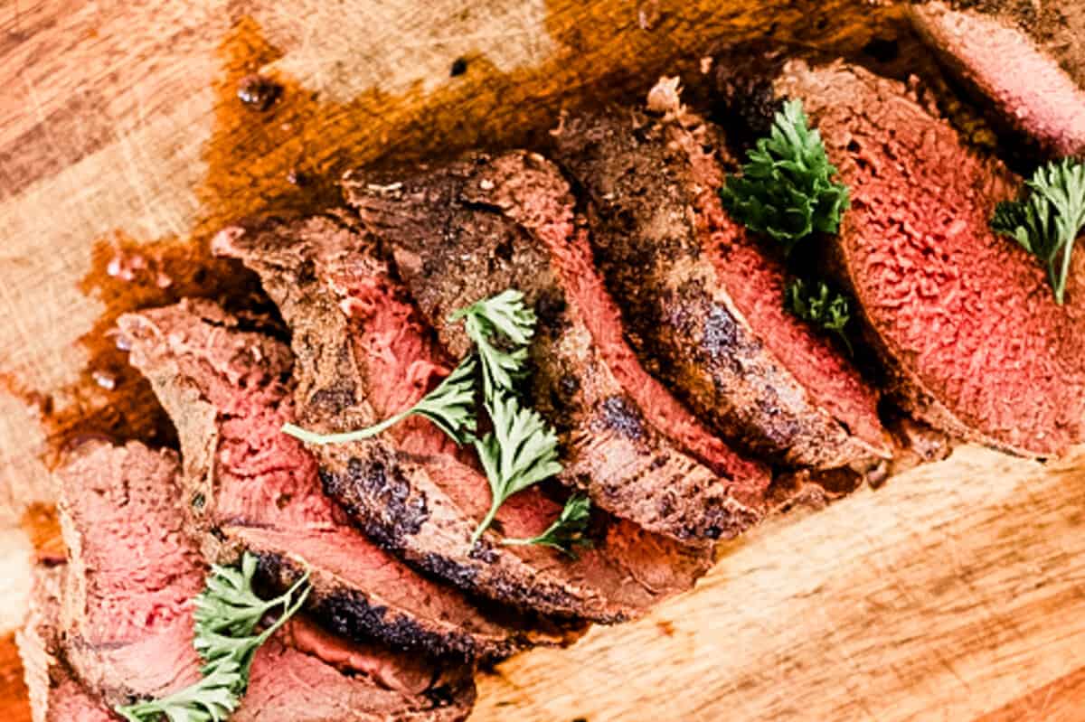 Thin sliced venison backstrap on a wooden cutting board.