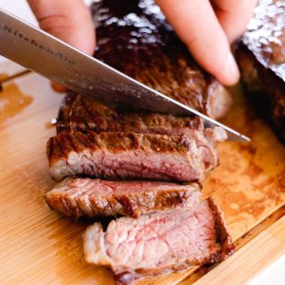 Slicing picanha steak with a sharp knife on a wooden cutting board.
