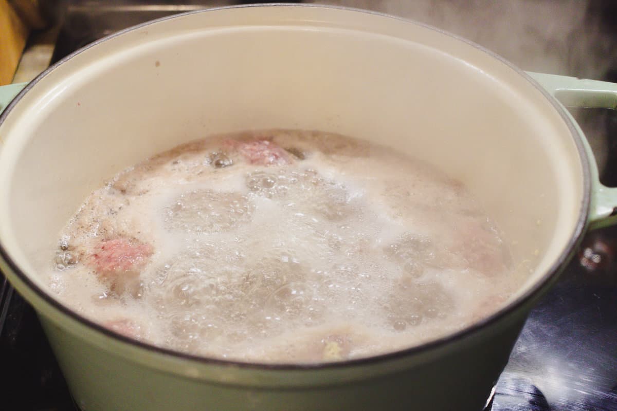 A white and green dutch oven full of vigorously boiling ground beef.