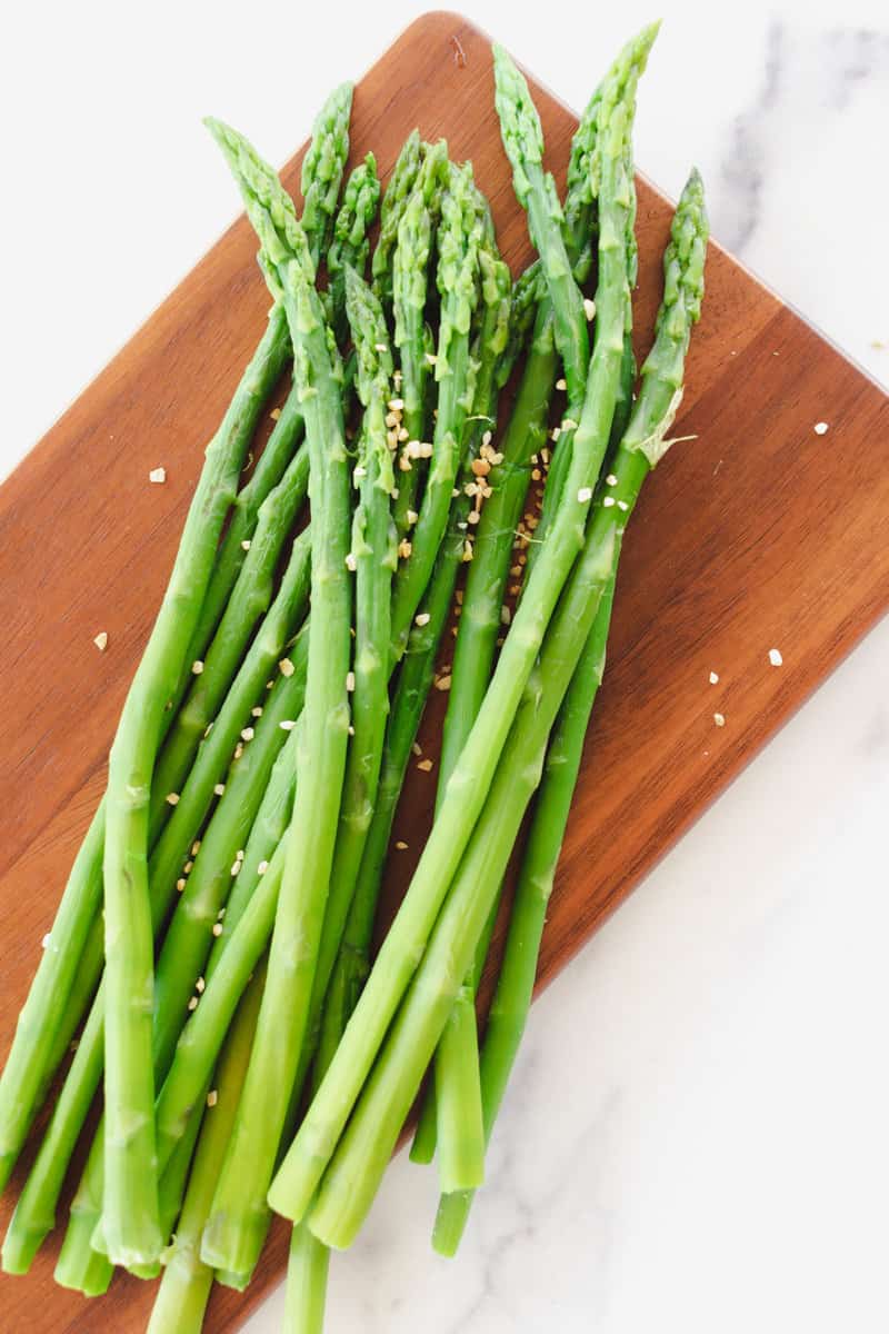 Boiled asparagus cooling on a wooden cutting board.